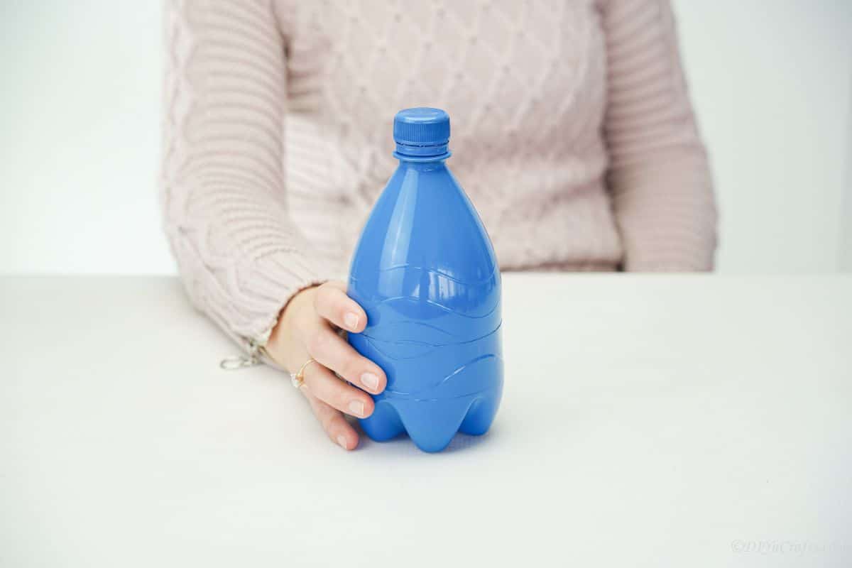 hand holding blue bottle on white table