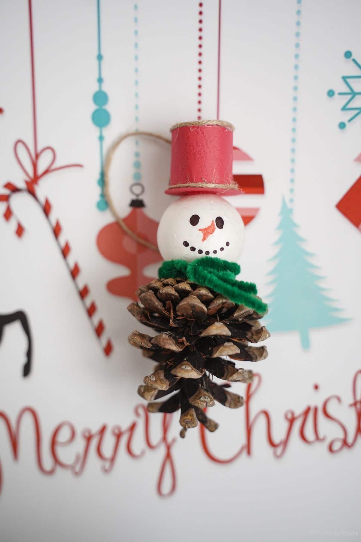 merry christmas paper behind pinecone snowman