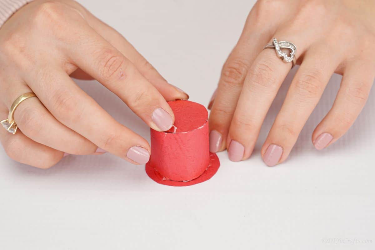 hand holding top hat made of red paper on white table