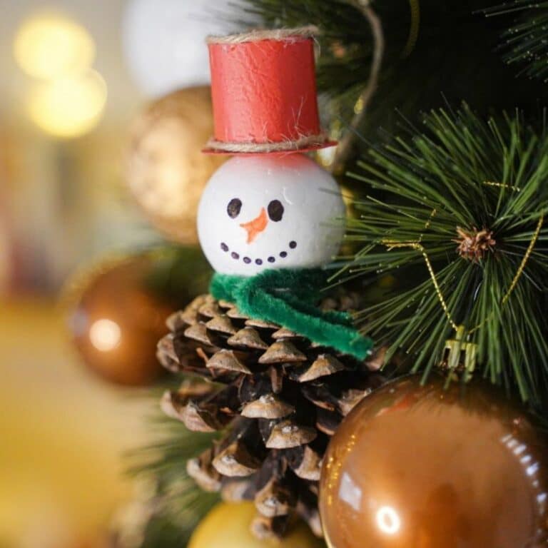 pinecone snowman ornament hanging in tree by gold bulb