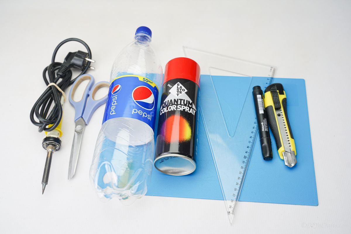 blue mat on white table with craft knife ruler spray paint and empty soda bottle