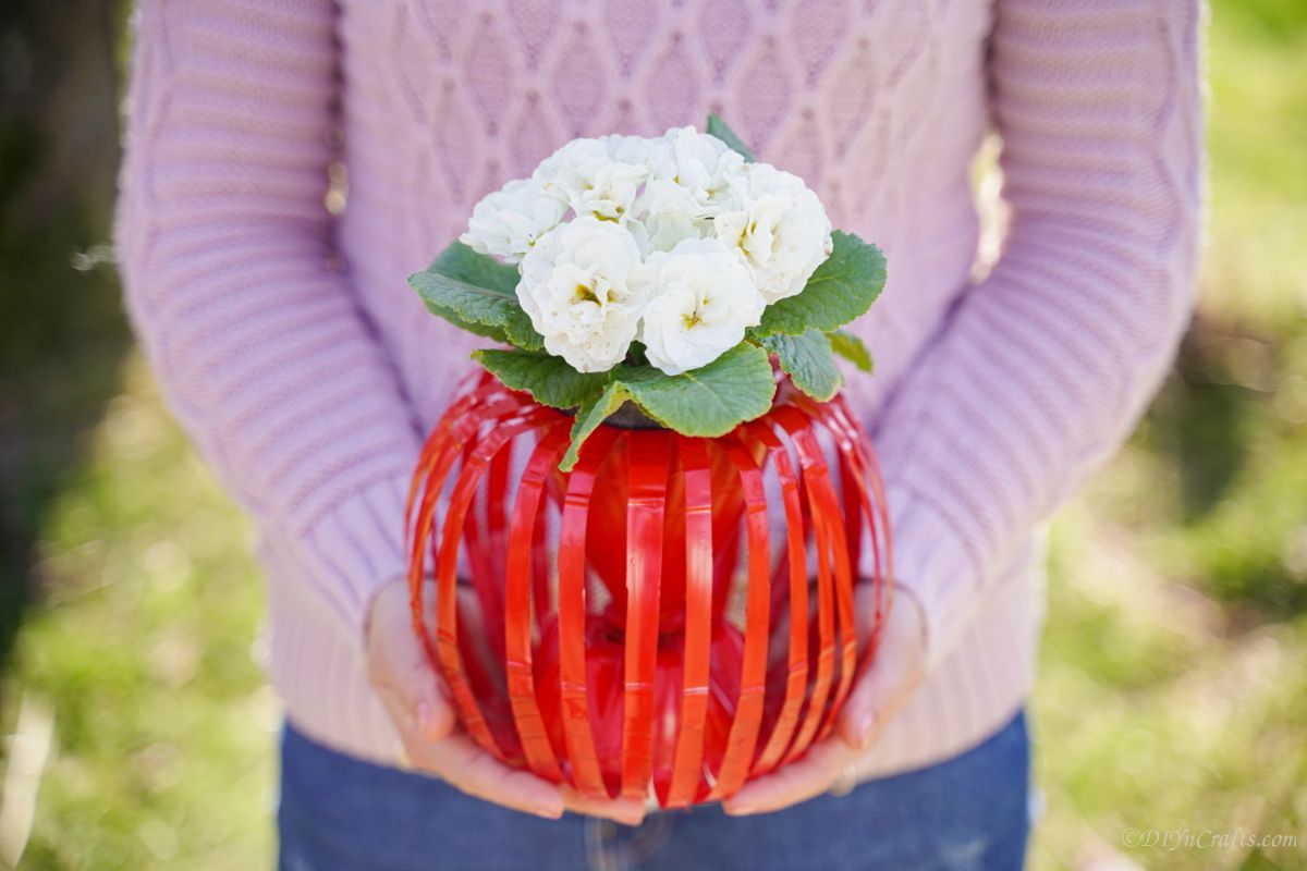woman in pink sweater holding red planter with white flowers