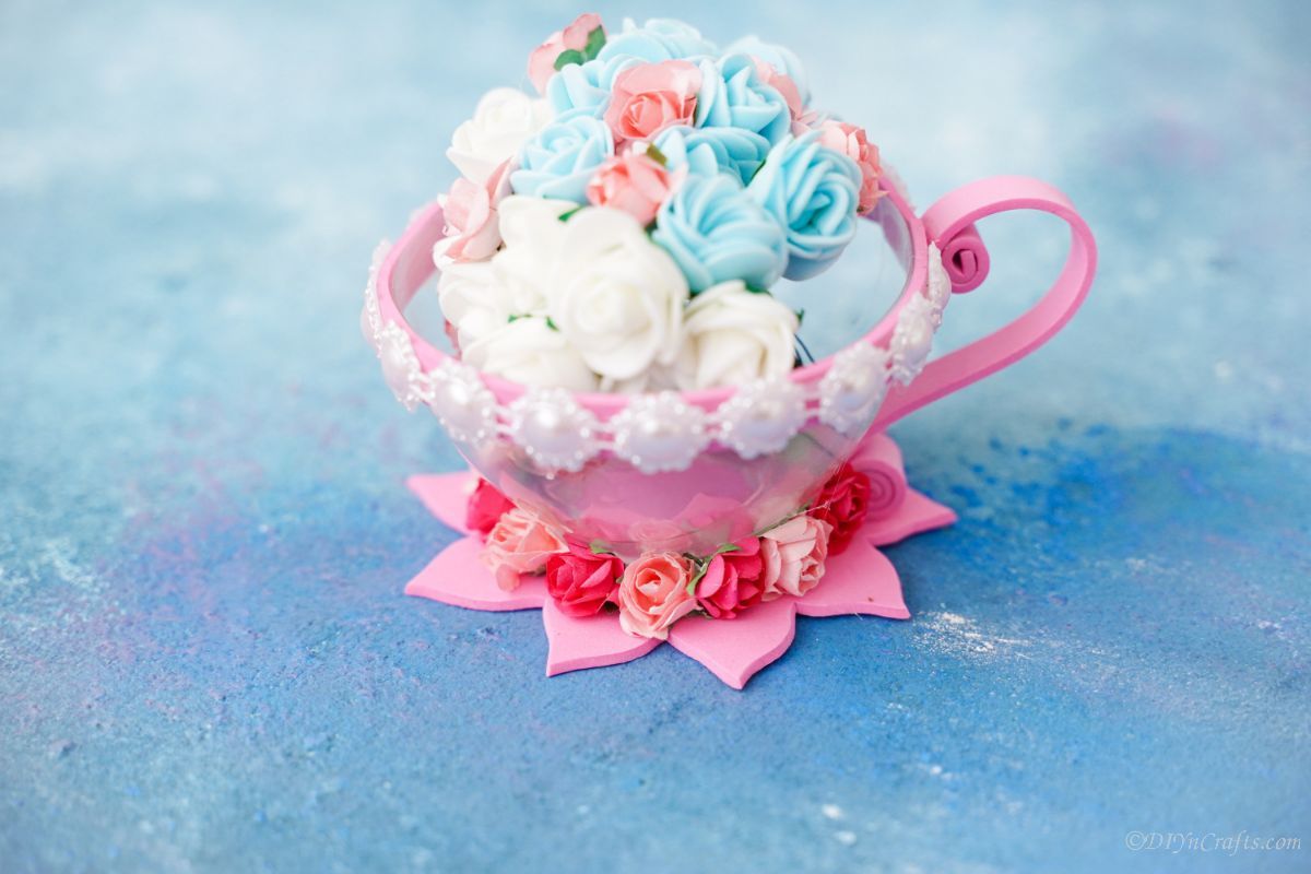 pink and white plastic teacup filled with fake white and blue flowers on blue paper