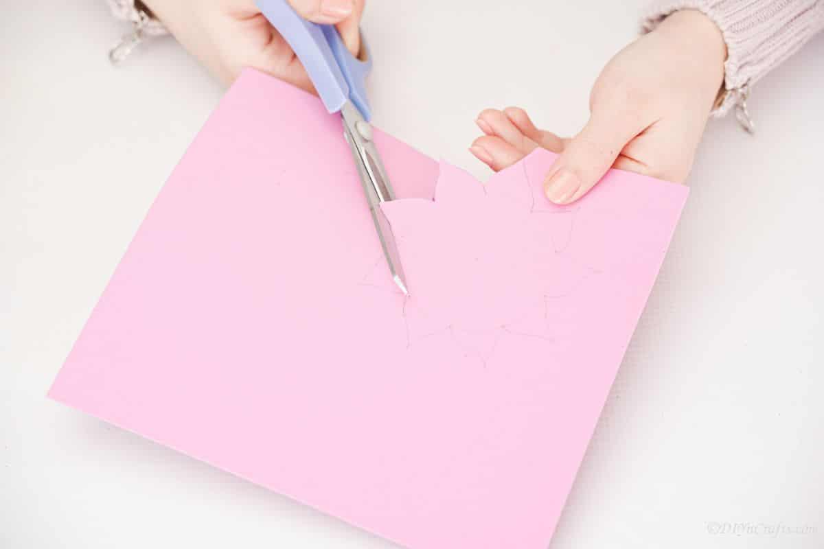 hand holding blue scissors cutting flower shape from pink foam
