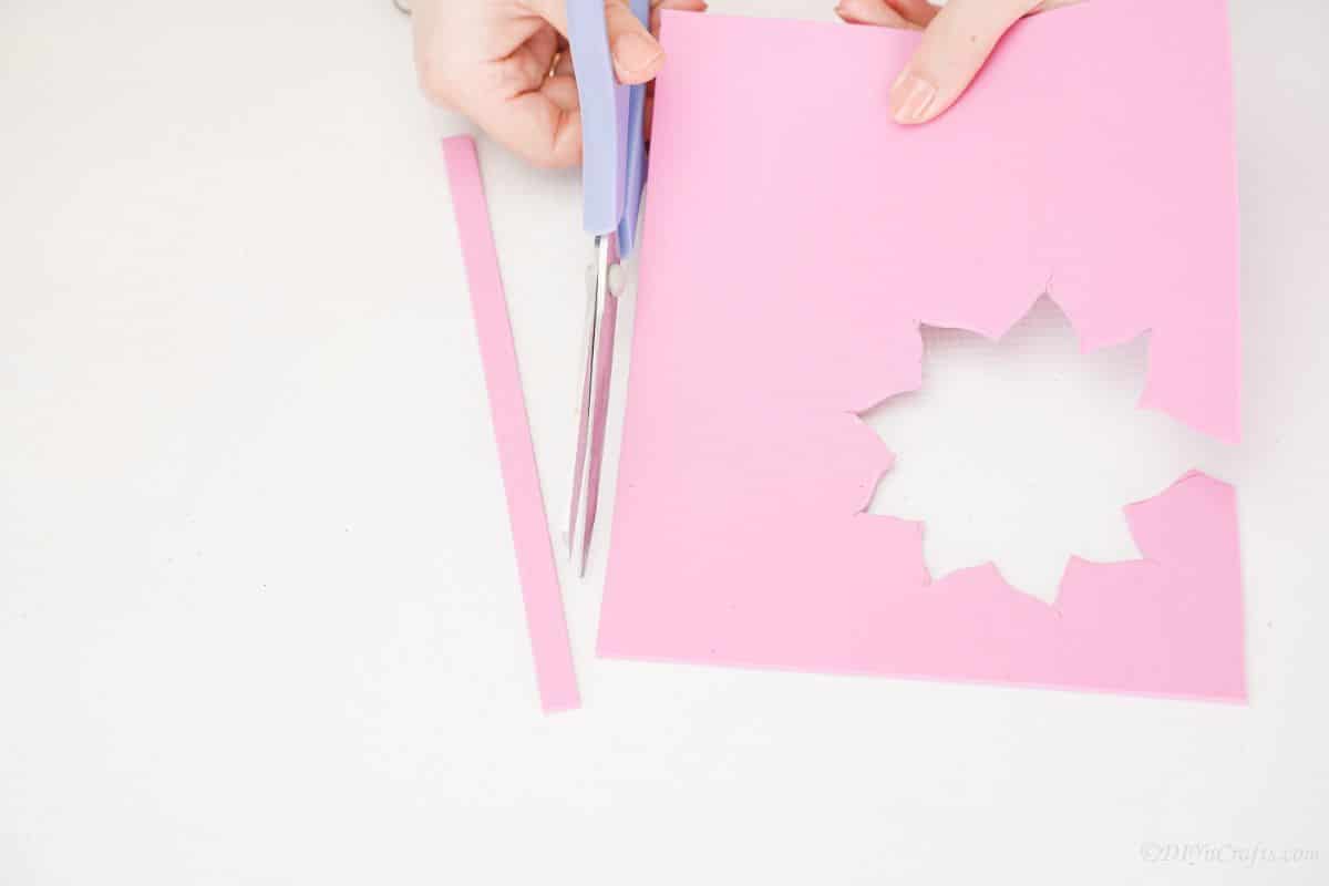 blue scissors cutting strips of pink foam