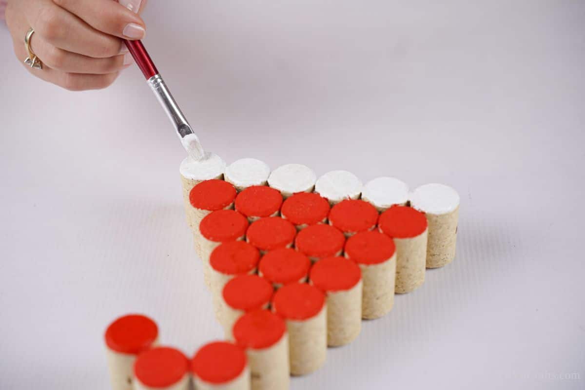 hand holding paintbrush to paint bottom row of cork on santa hat decoration