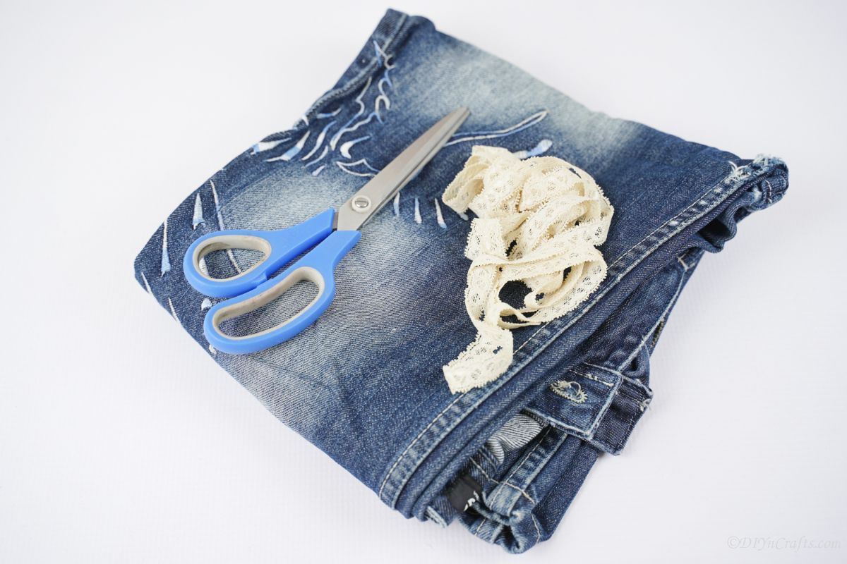 folded blue jeans on white table with blue scissors and lace ribbon