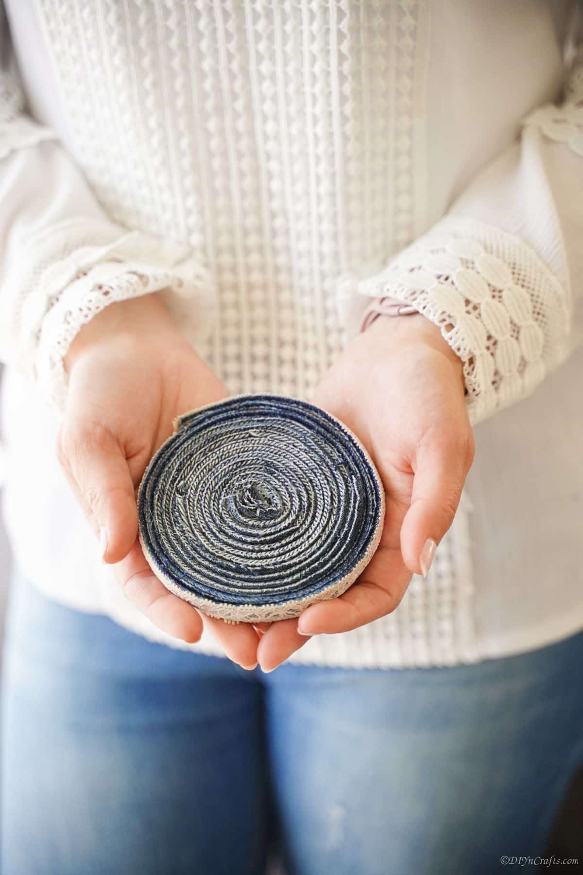 lady in white and jeans holding old blue jeans coaster in her hands