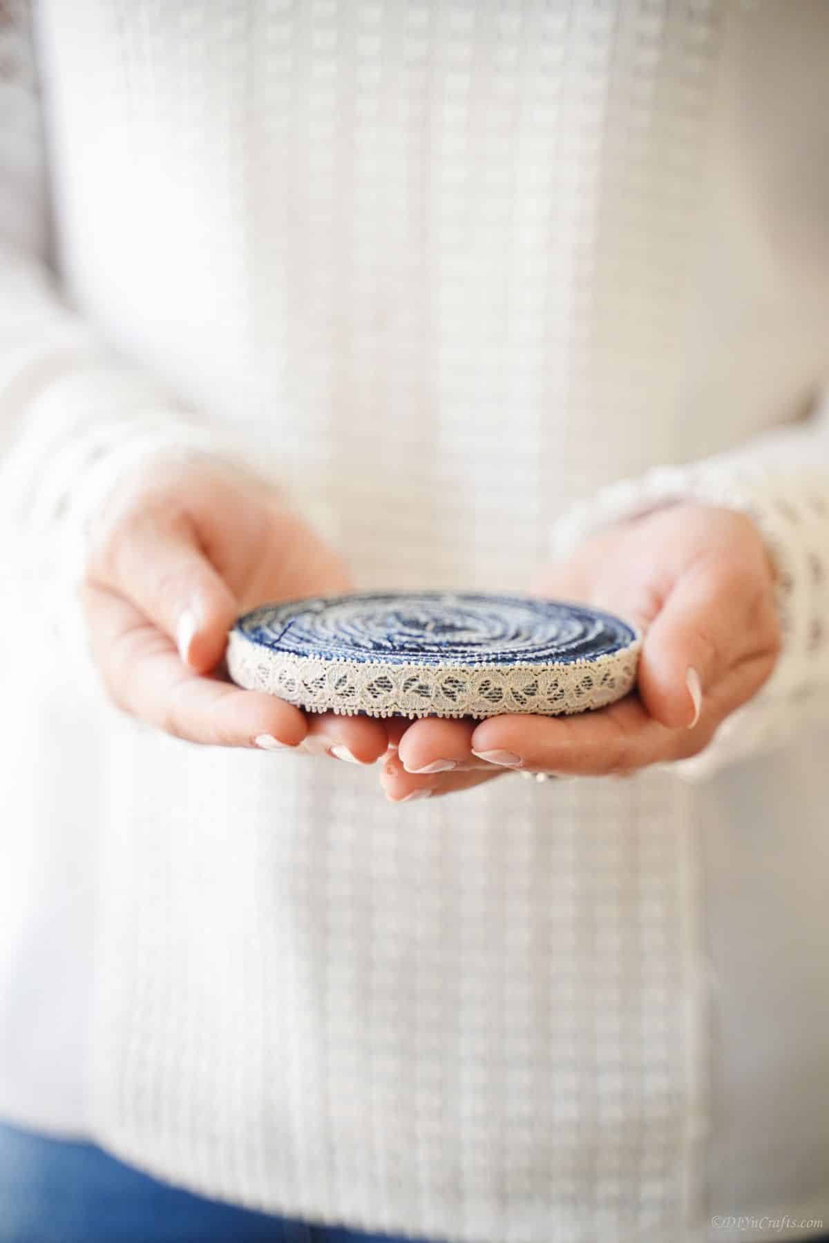 lace edged blue jeans coaster in hands of woman in white sweater