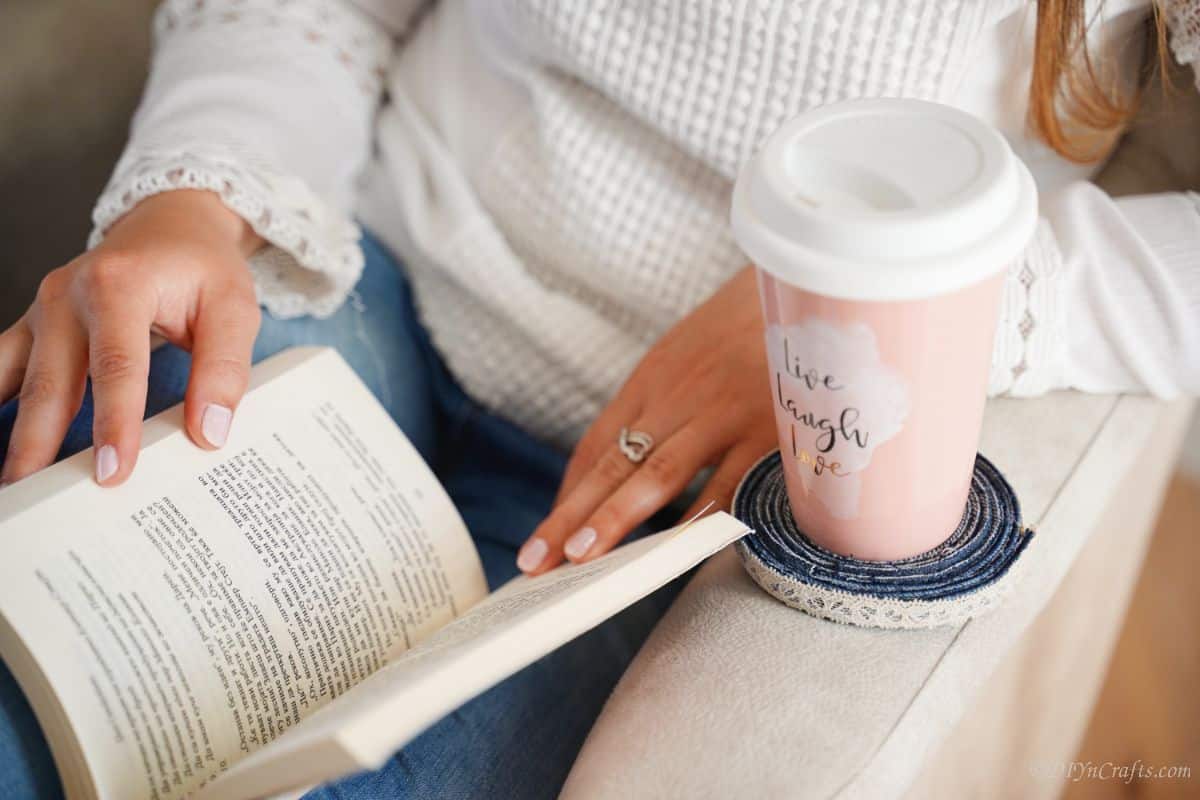 pink travel mug on blue jeans coaster on the edge of a white chair with woman sitting