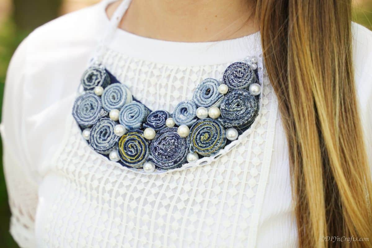 lady with brown hair wearing a denim necklace over white shirt