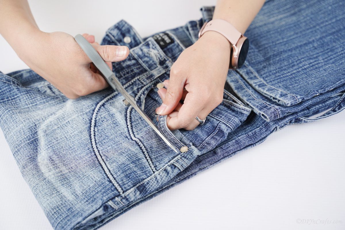 hand holding gray scissors to cut through pocket seam on blue jeans