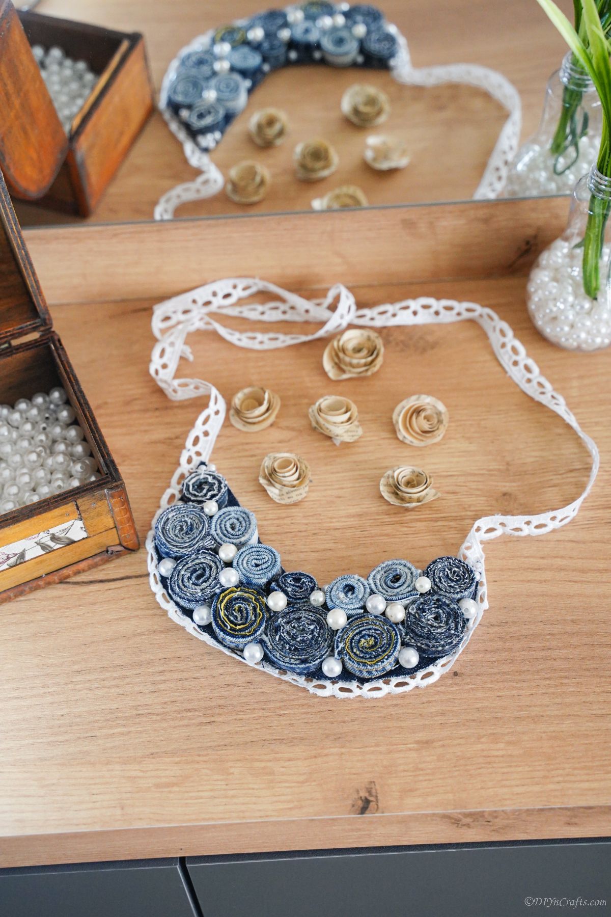 old blue jeans necklace laying on table by box of beads