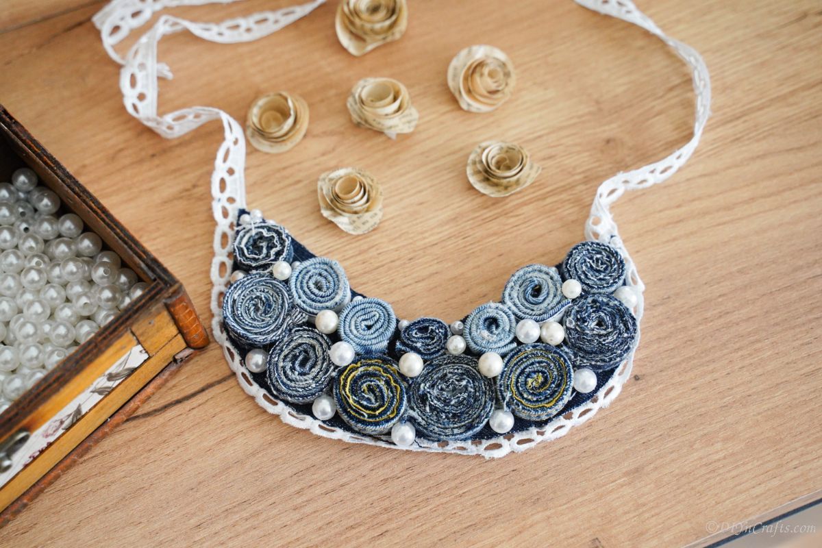 denim and lace necklace on wood table by paper flowers
