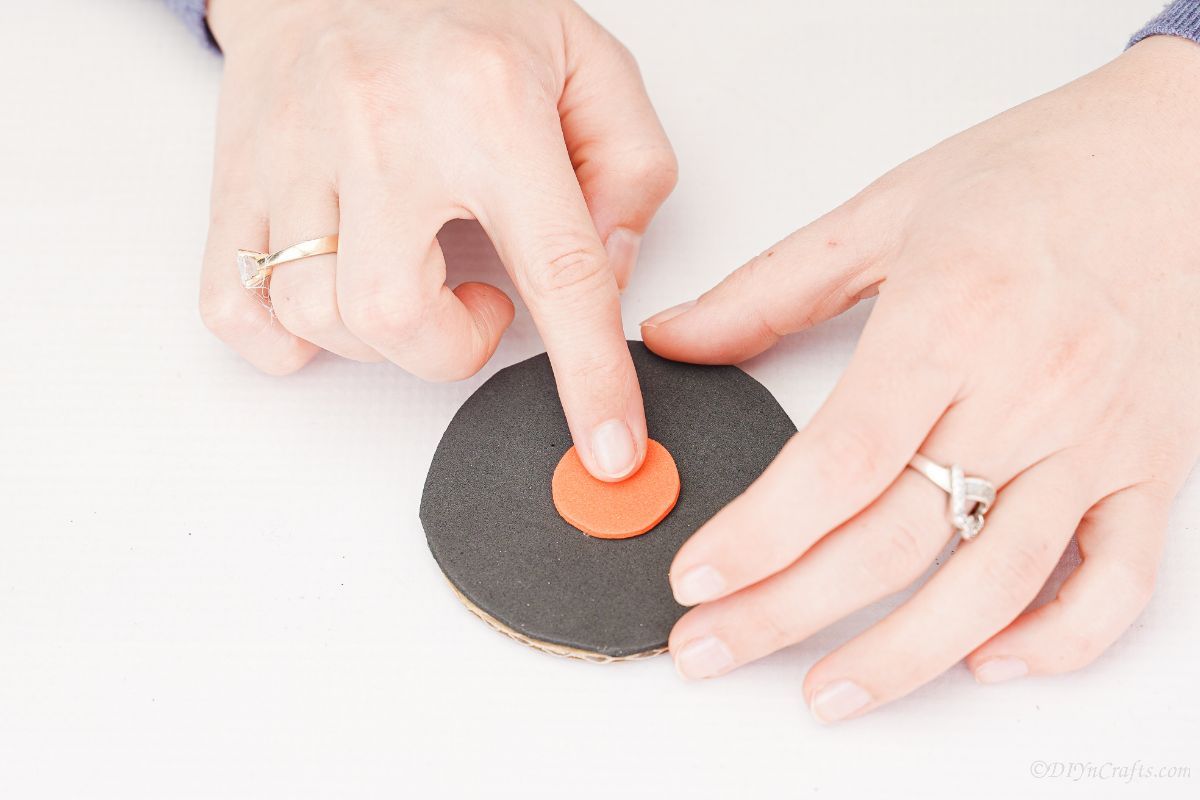 finger holding orange circle in the middle of black wheel