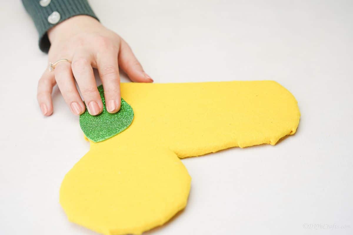 green foam paper being held on edge of yellow caterpillar body