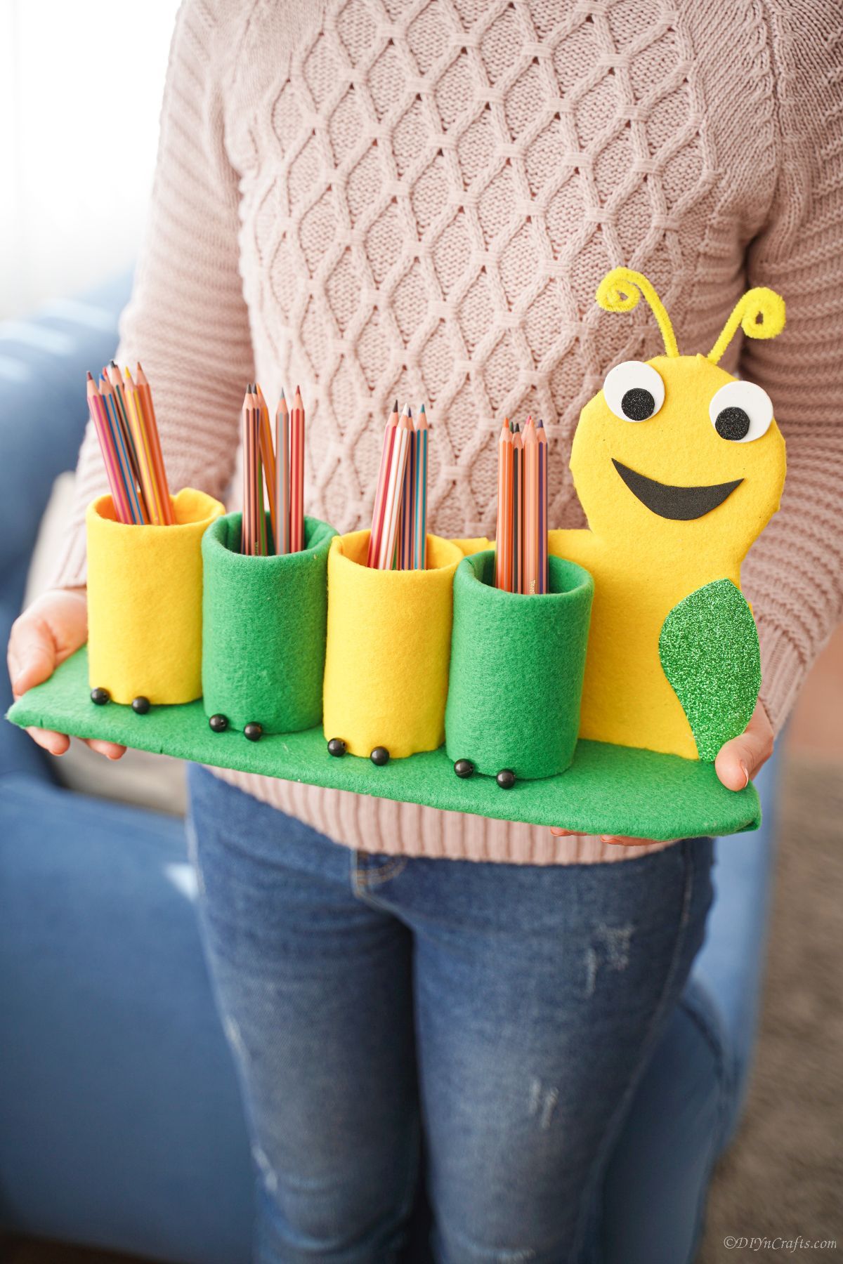 woman in pink holding green and yellow caterpillar pencil holder