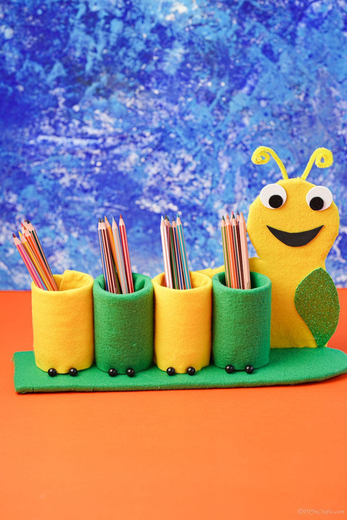 yellow and green caterpillar pencil holder in front of blue background on orange table
