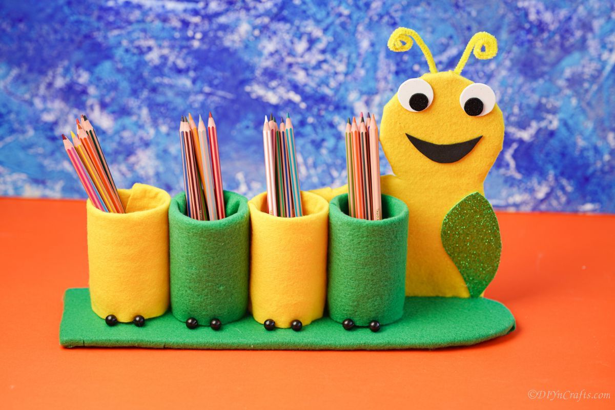 yellow and green caterpillar pencil holder in front of blue background on orange table