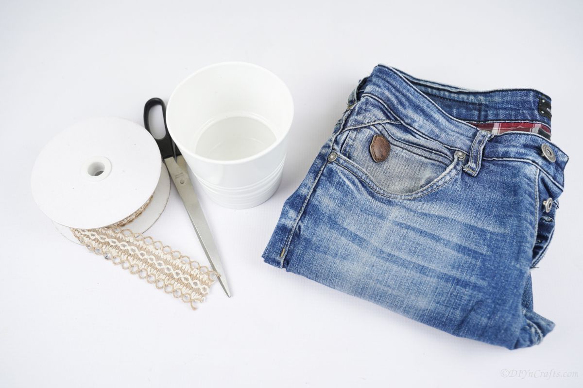 folded blue jeans on white table next to spool of ribbon and scissors