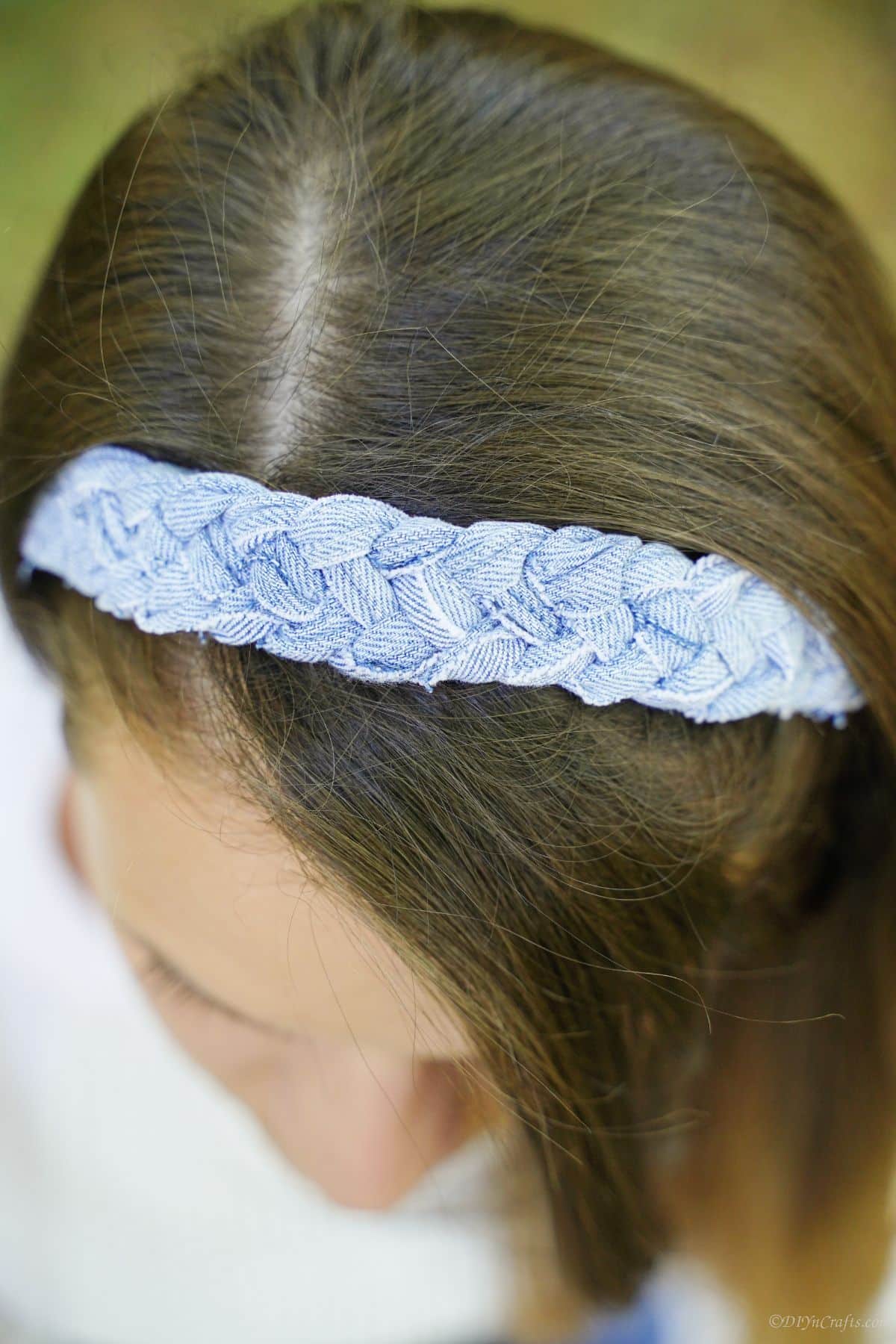 looking down at the top of a braided denim headband being worn by a woman with brown hair