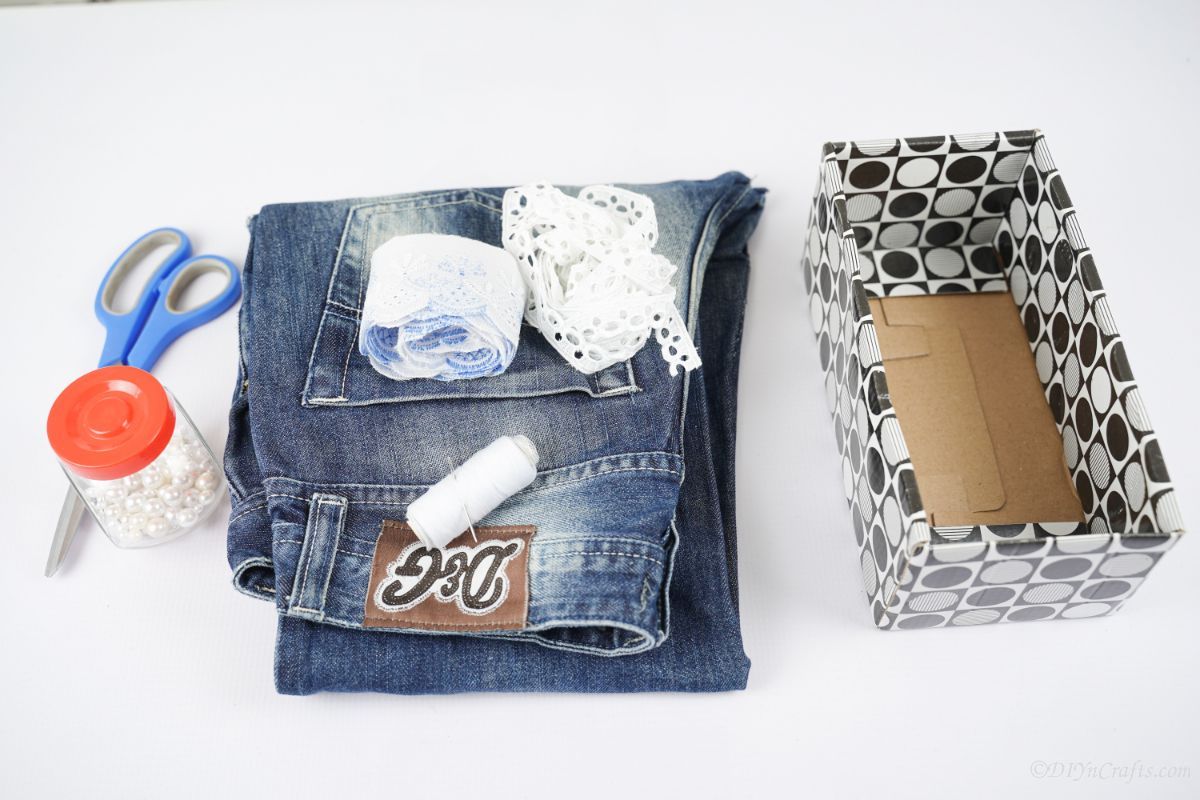 box on table next to folded blue jeans roll of lace and scissors