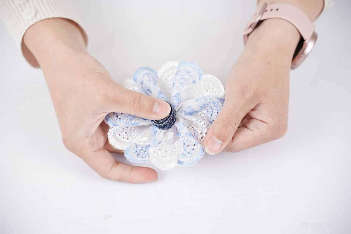hand holding denim circle to center of white lace bow