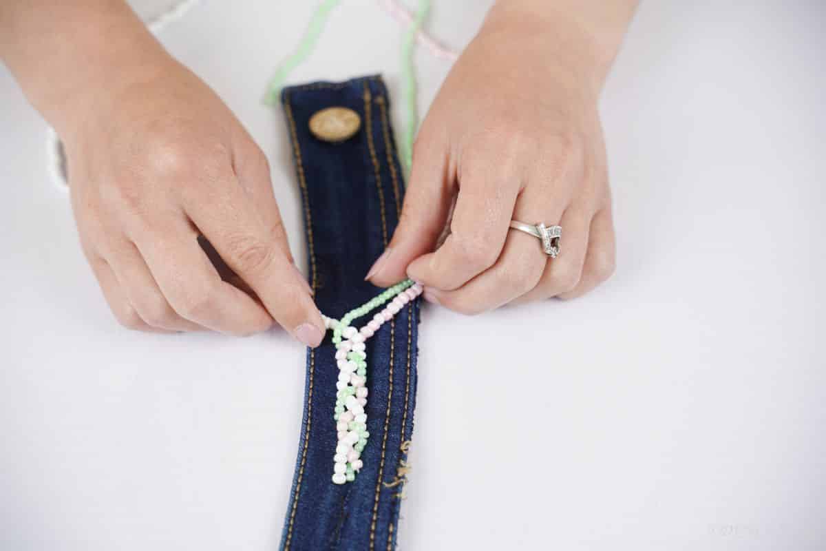 hands braiding strands of beads attached to denim