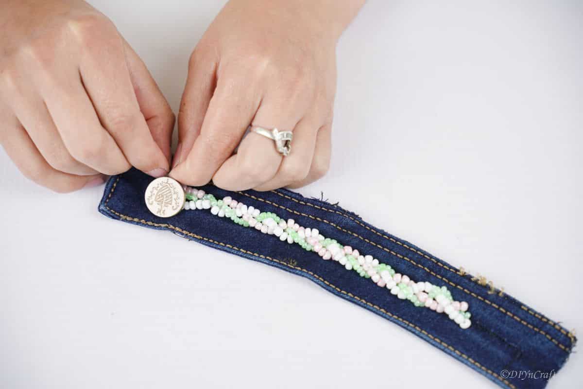 hand tying string of beads around button on denim strip