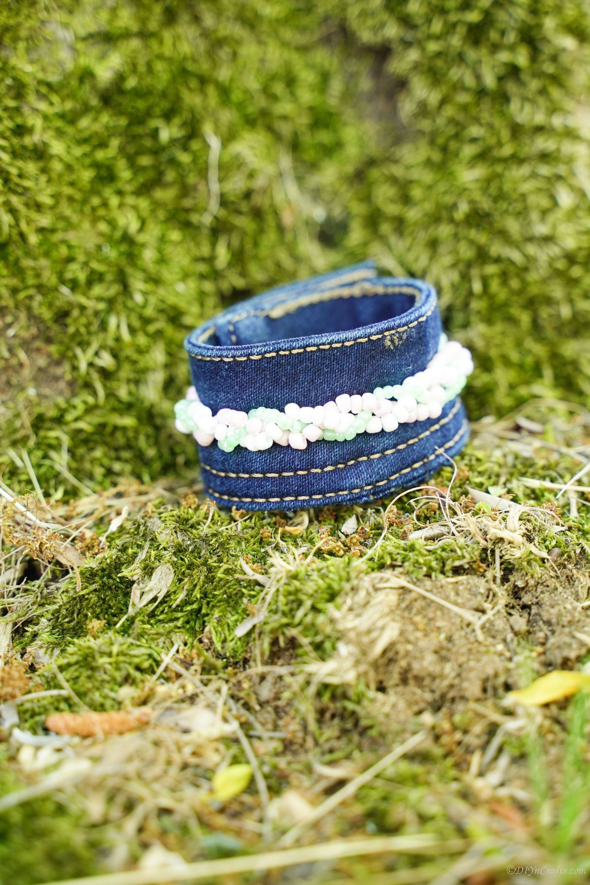 braided beads on the outside of a blue jean cuff bracelet sitting in the grass