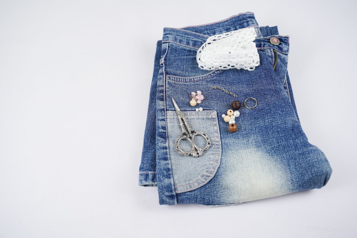folded blue jeans on white table with scissors and beads on top