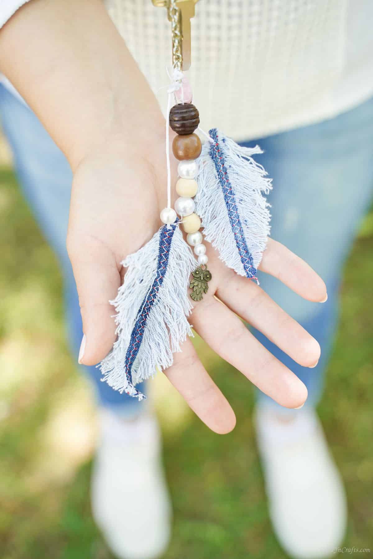 denim feather keychain laying over top of hand