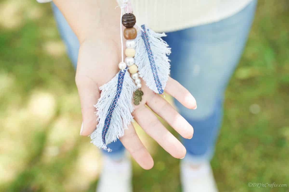 woman holding denim and bead feather keychain