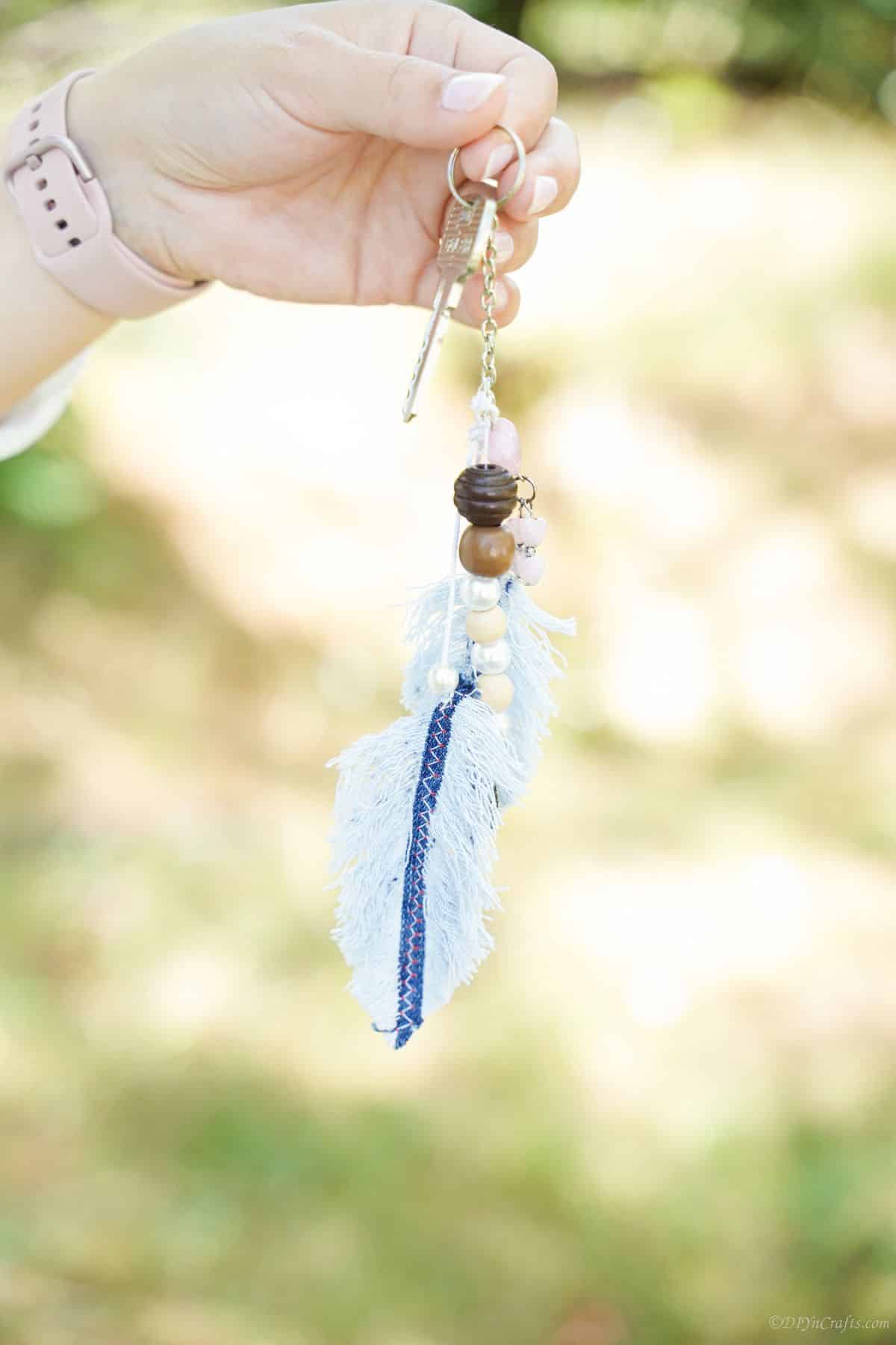 hand holding denim feather keychain outside