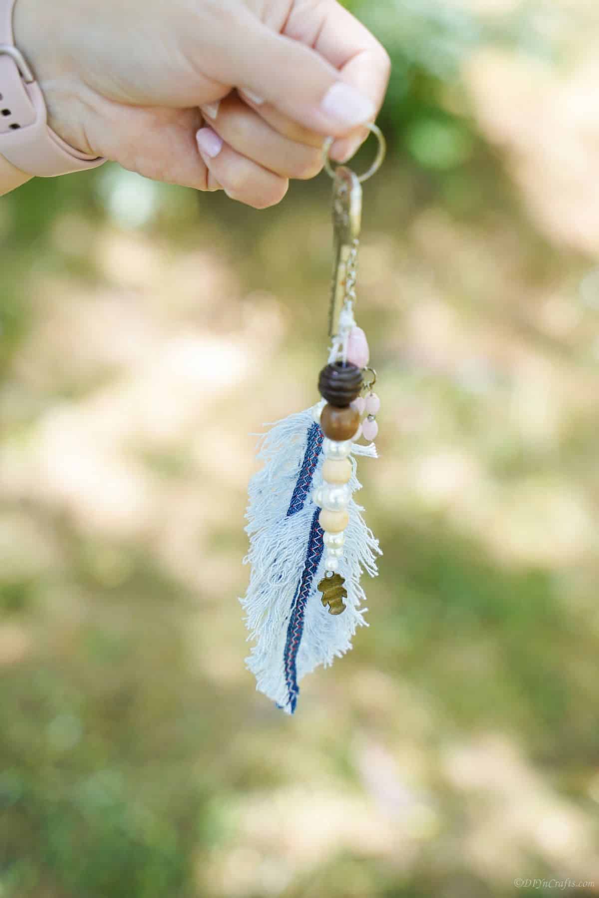 beaded old blue jeans feather keychain being held by hand in front of grass