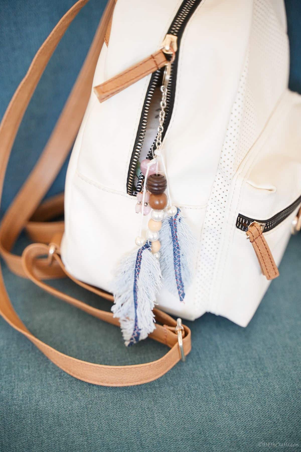 denim feather keychain hooked on side of white backpack purse