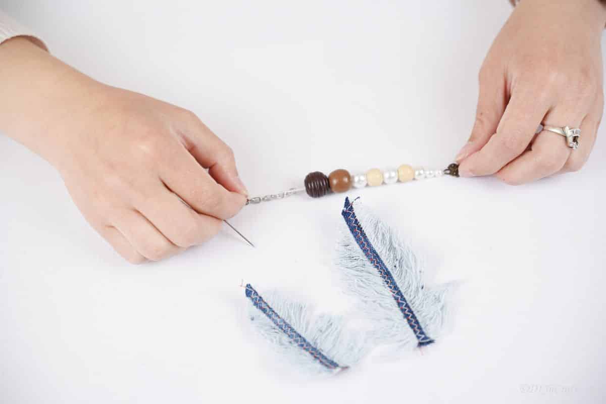 a thread of wood beads being held above feather denim pieces