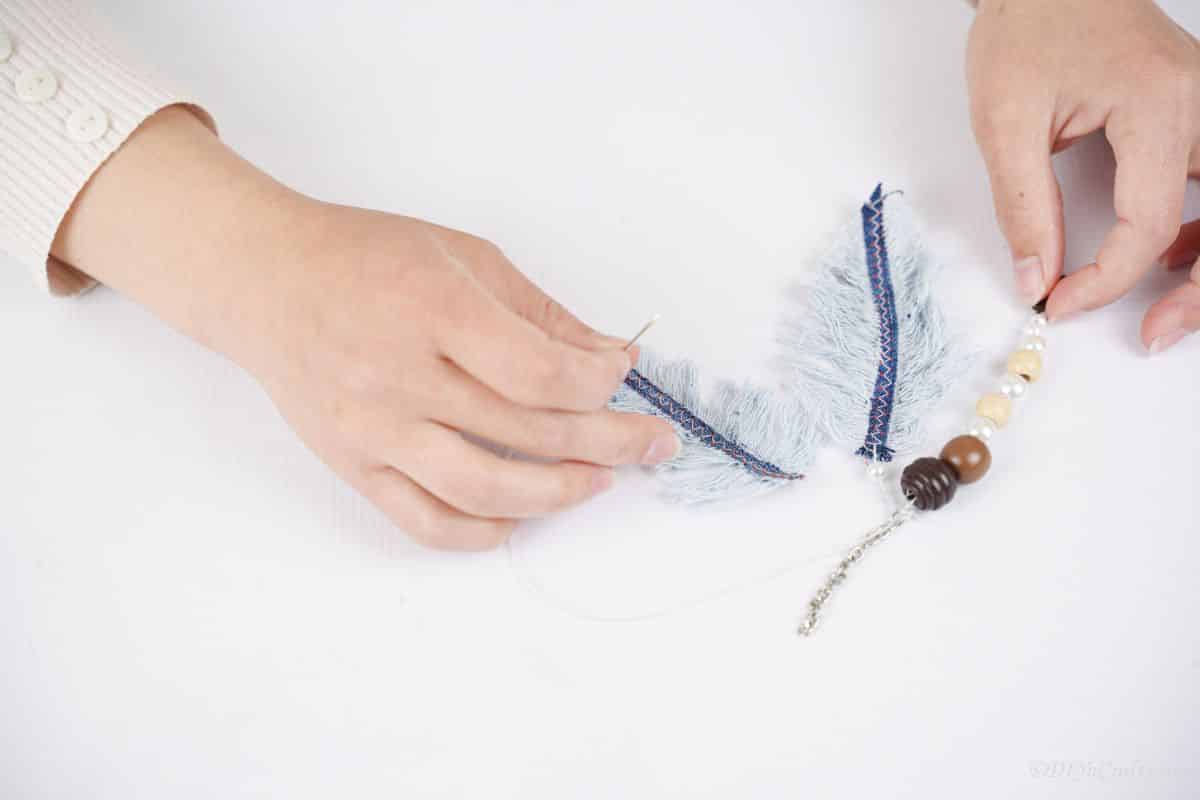 hand connecting the denim feathers to the beads