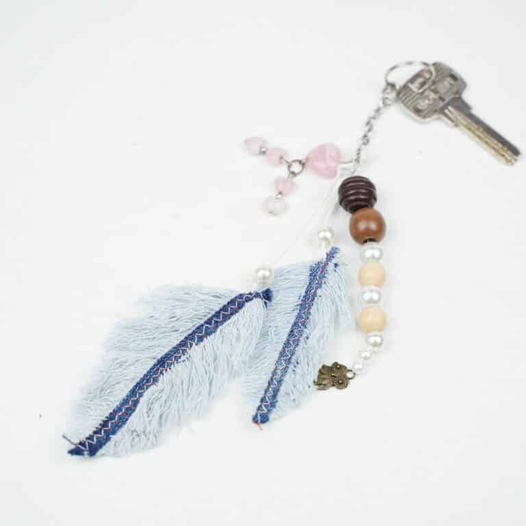 beaded keychain with old blue jeans feathers on bottom laying on white table