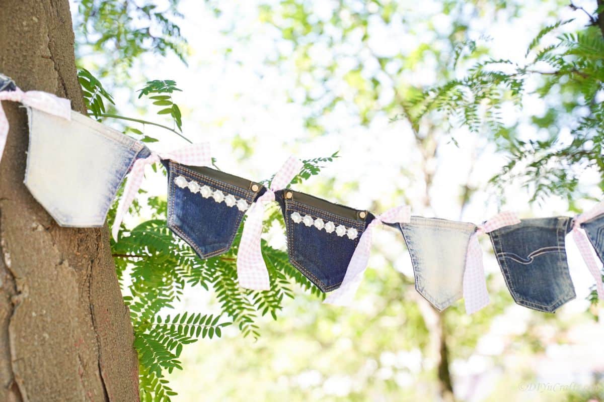 pockets from old blue jeans sewn together as a garland hanging on a tree outside
