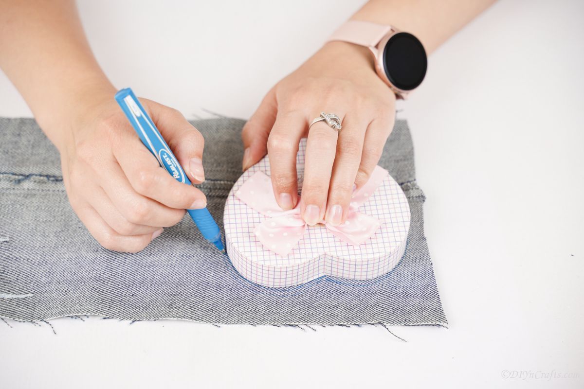 blue pen being used to trace around small heart shaped box onto denim