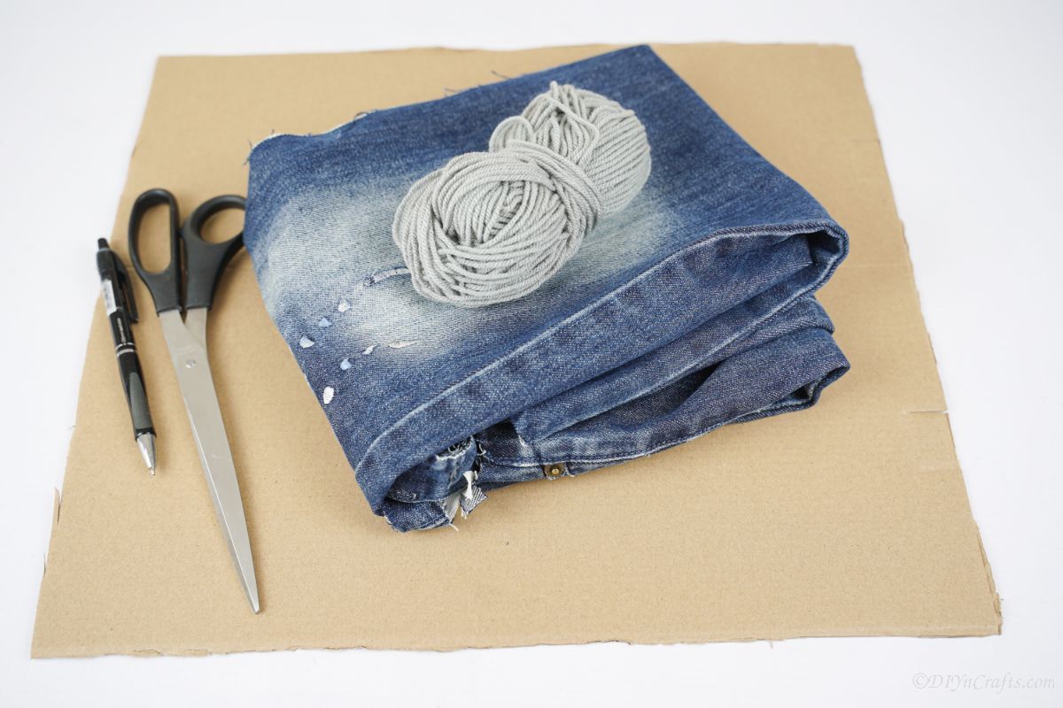 folded blue jeans on cardboard with yarn and scissors