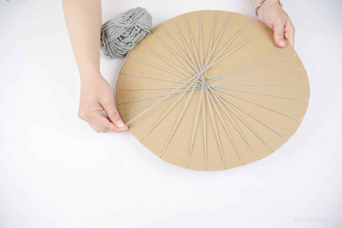 gray yarn being wrapped around cardboard circle