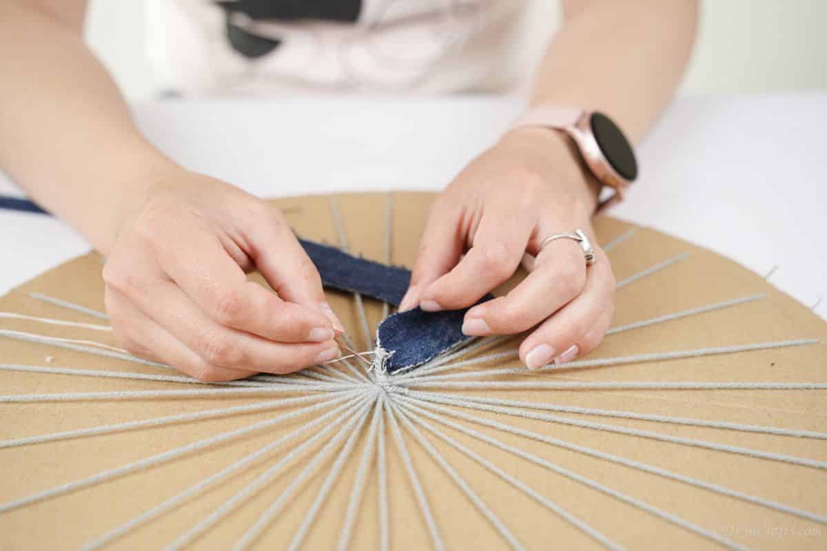 hand sewing denim strip onto yarn on cardboard