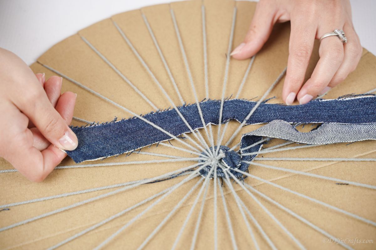 srip of denim being woven around circle of yarn on cardboard