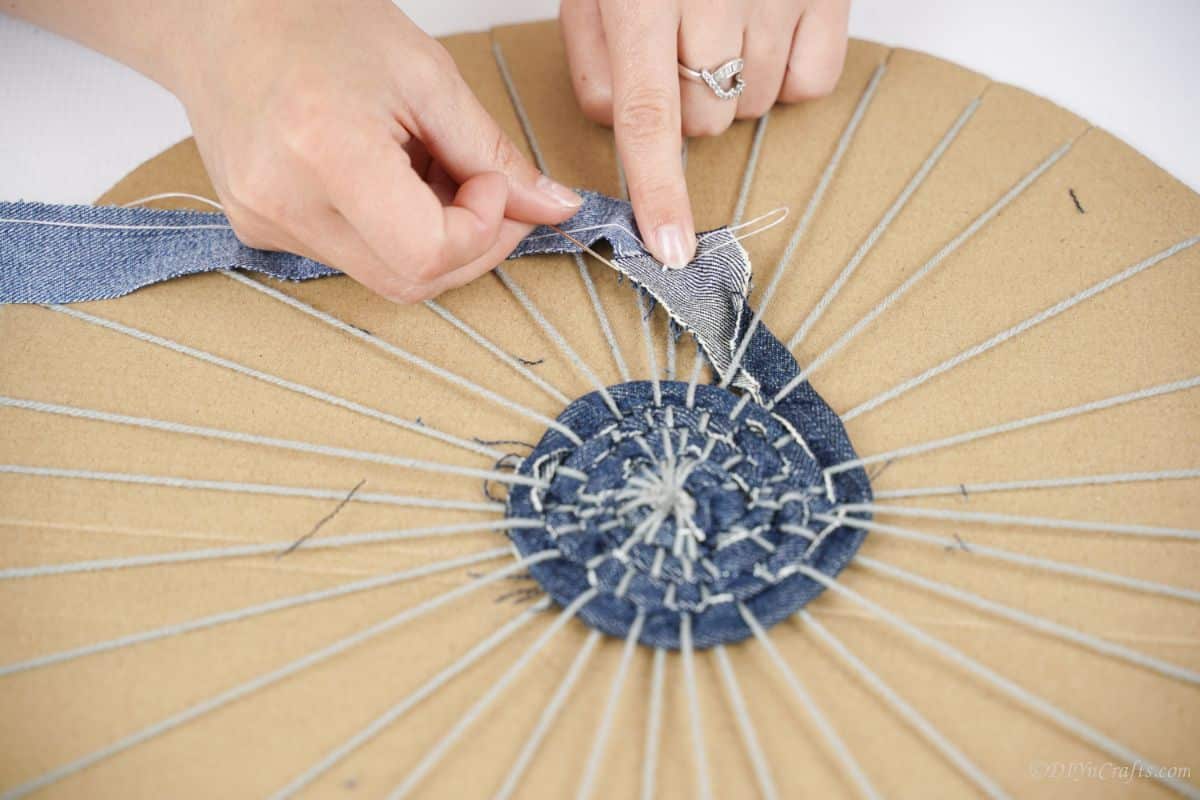 hand sewing two denim strips together while weaving under yarn