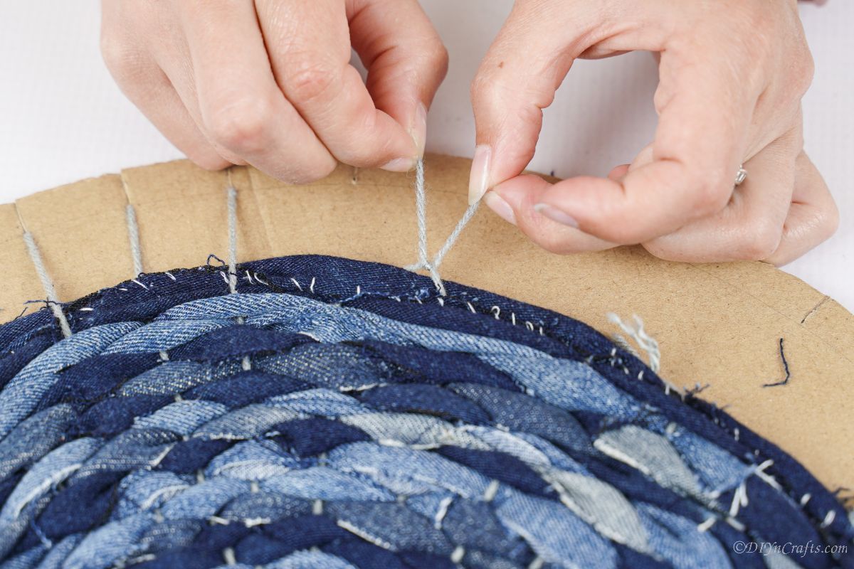 hand tying gray yarn on edge of cardboard circle of denim