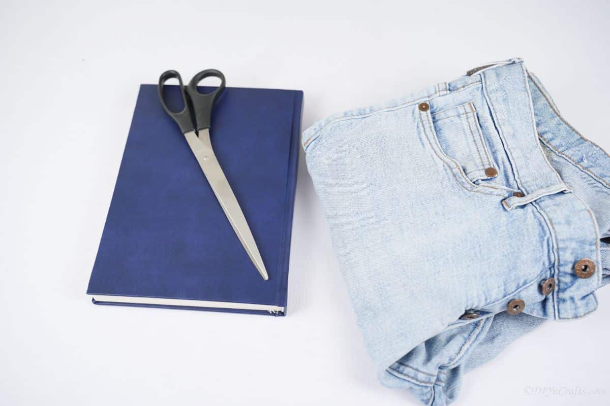 blue book with black scissors on table with folded blue jeans