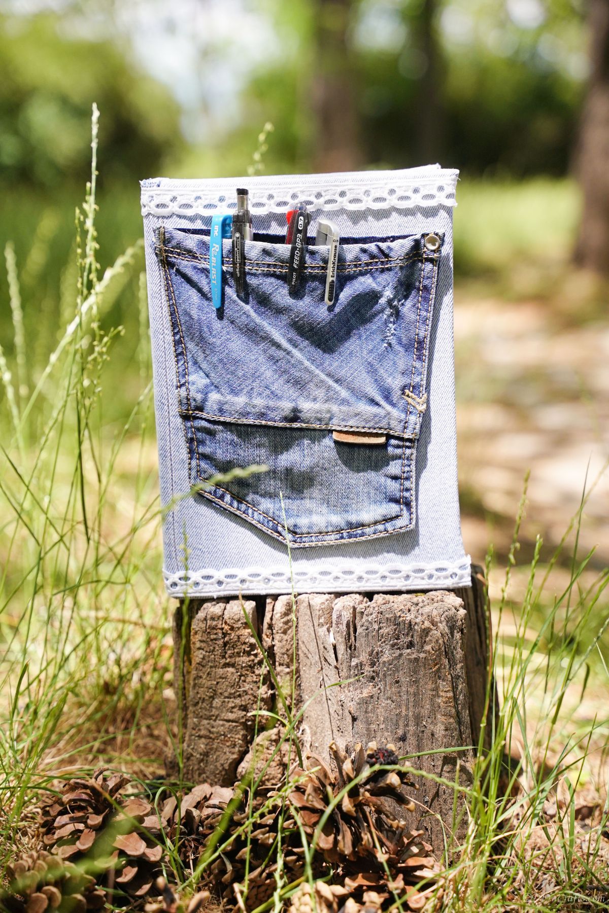 denim covered book with pens in pocket on front standing on tree stump