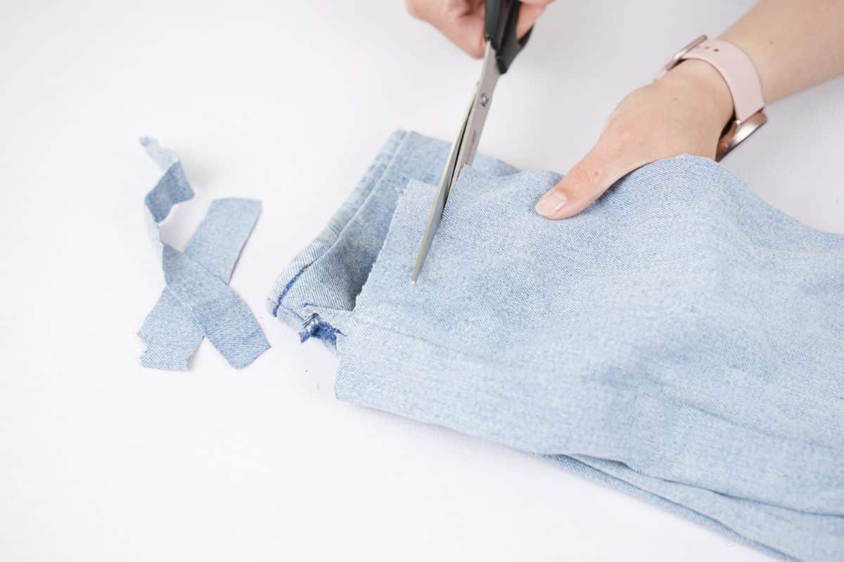 black scissors cutting blue jeans into strips